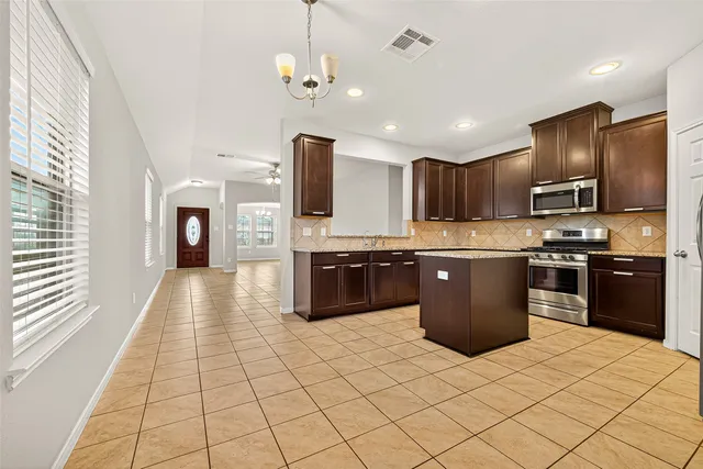 a large kitchen with stainless steel appliances granite countertop a stove top oven a sink dishwasher a refrigerator and a cabinets