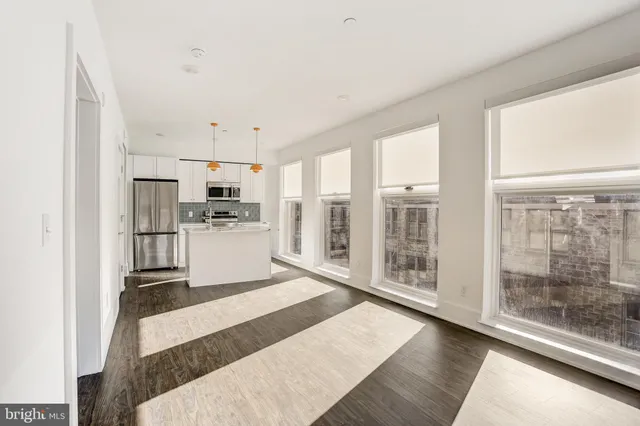 a large white kitchen with granite countertop a refrigerator a stove a sink and white cabinets with wooden floor