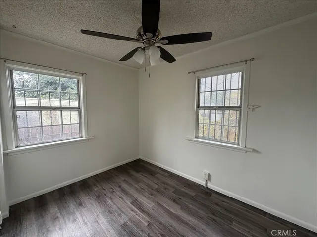 an empty room with wooden floor fan and windows