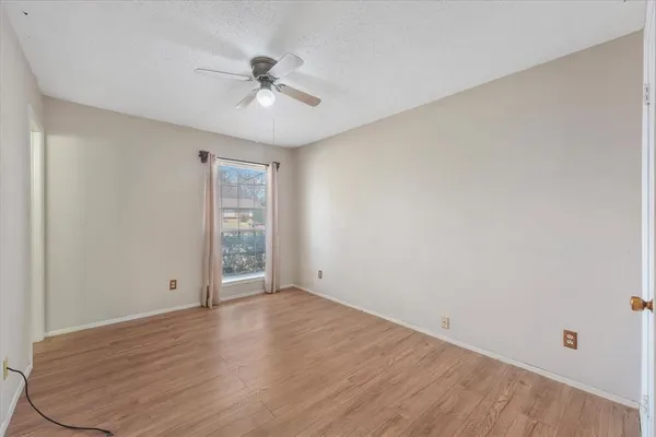 a view of an empty room with wooden floor and a ceiling fan