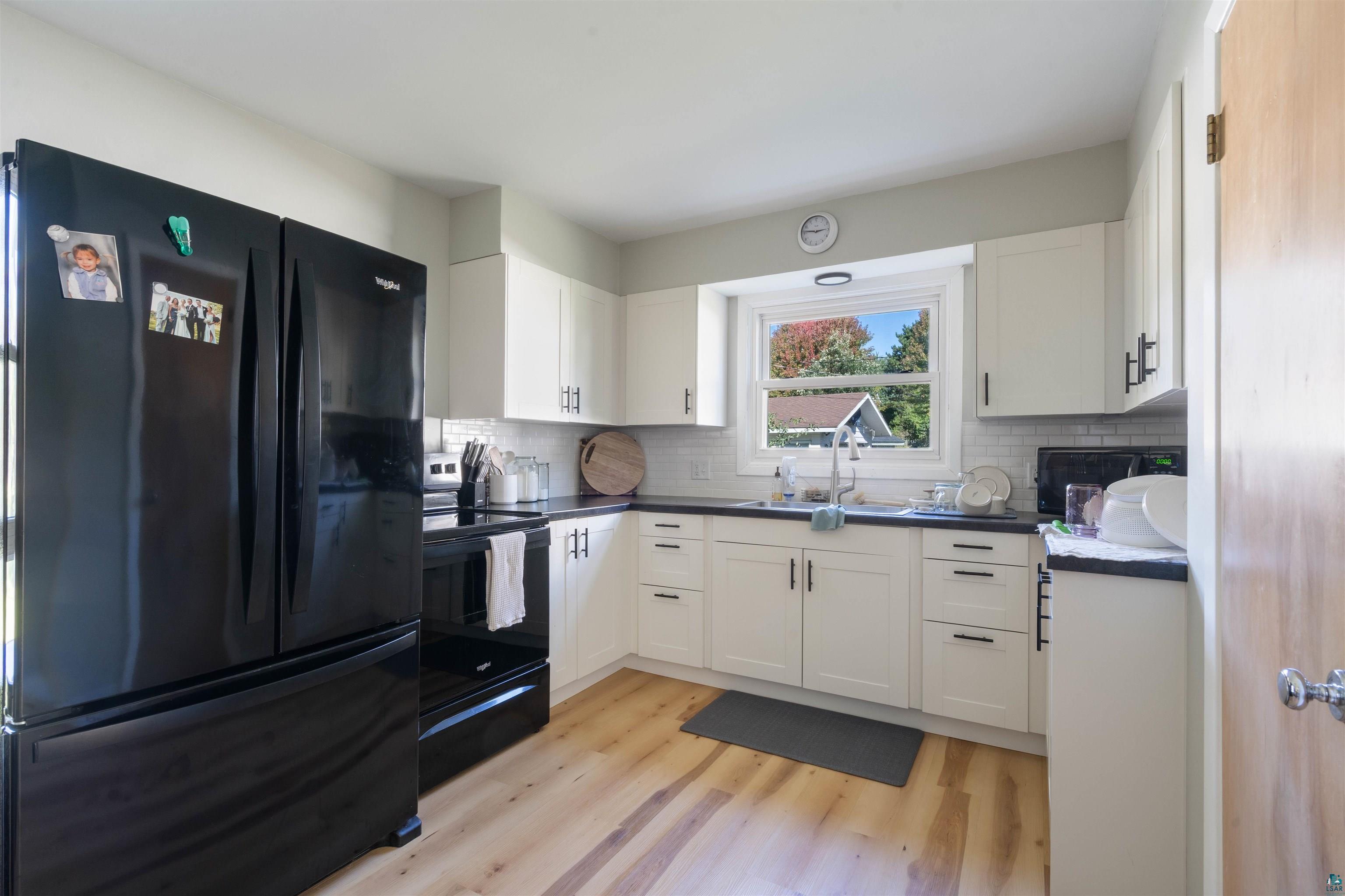 3715 Rendle Avenue Duluth, MN 55803 - Photo 17 of 20 White cabinetry with black hardware, wood-finish flooring, a black appliance suite, and a white subway tile backsplash