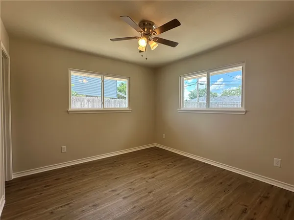 a view of an empty room with wooden floor and a ceiling fan