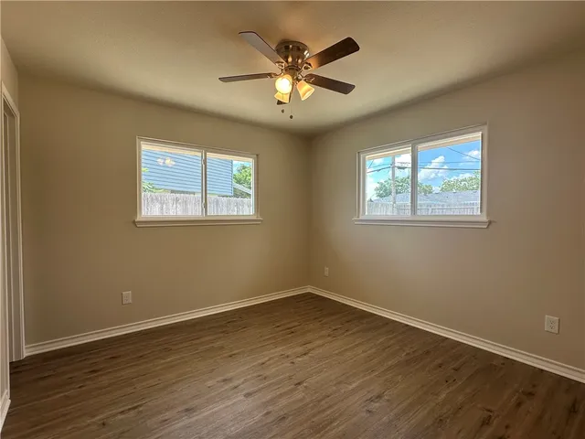 a view of an empty room with wooden floor and a ceiling fan