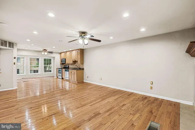 a view of an empty room with wooden floor and a kitchen