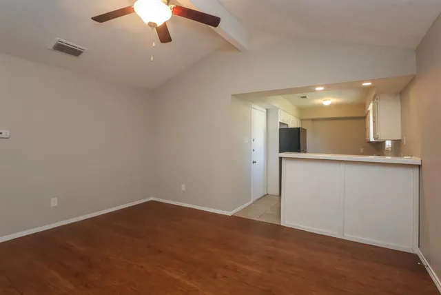 a view of an empty room with wooden floor and a kitchen