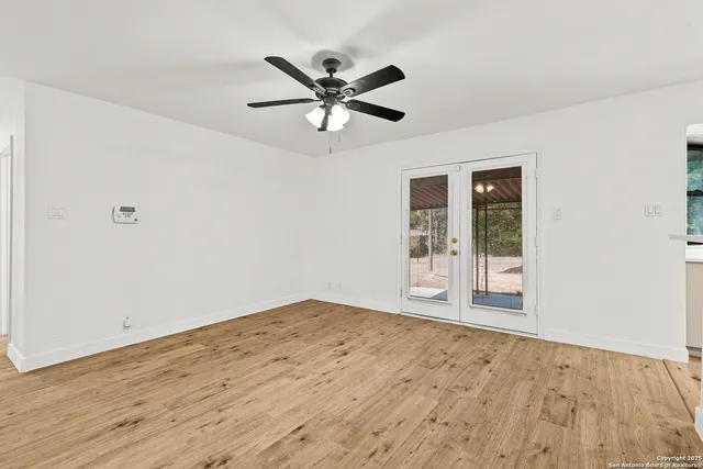a view of an empty room with wooden floor and a ceiling fan