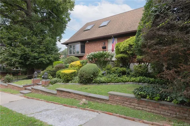 a brick house with a yard plants and large tree