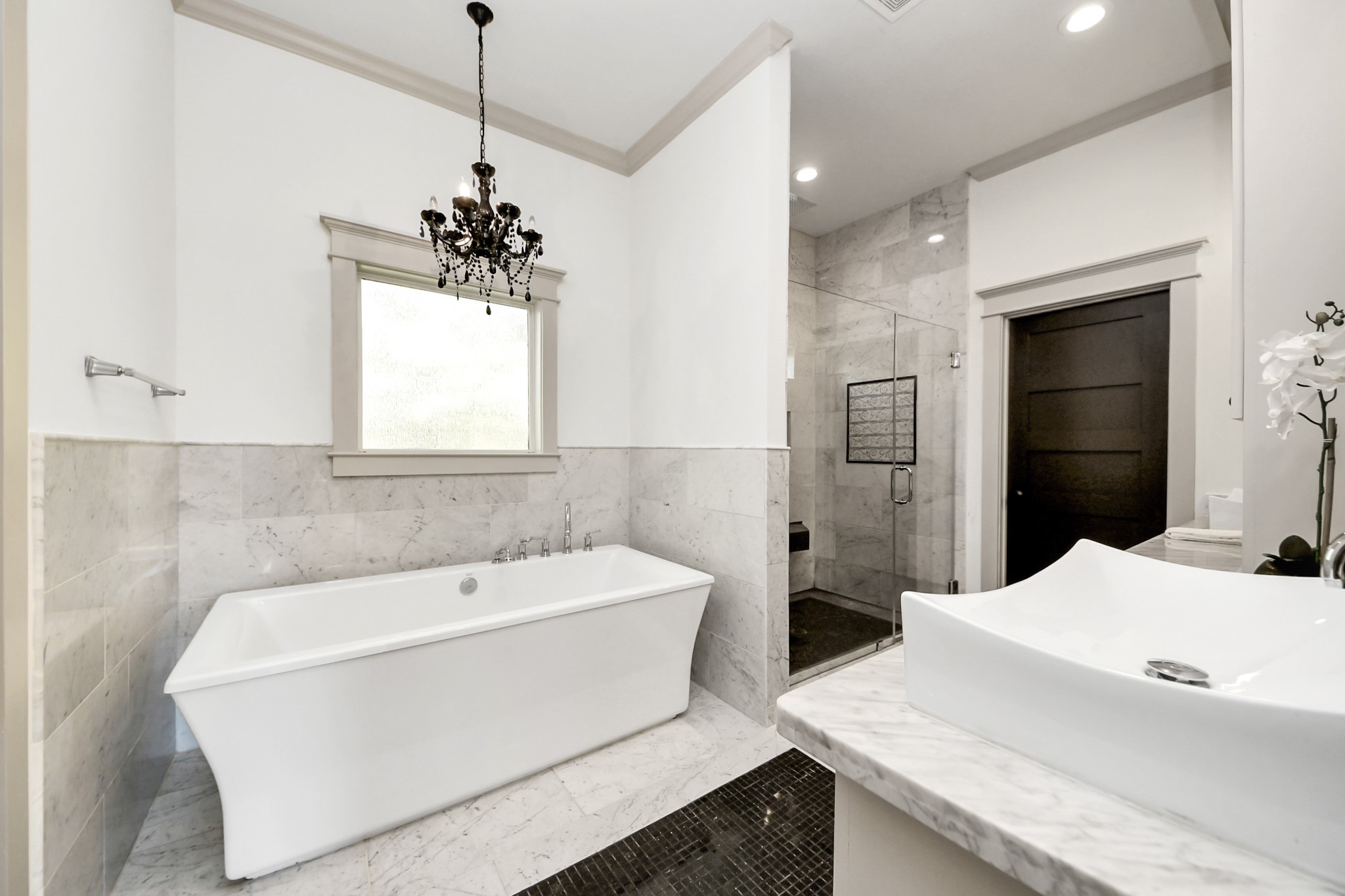 1202 Archer Street Houston, TX 77009 - Photo 26 of 46 Tailor-made bath features a modern, freestanding soaking tub, a glass-enclosed frameless shower, and a stylish vanity with vessel sinks. A decorative chandelier and ornate mirror add elegance, while natural light filters through the window, enhancing the bright, clean design.