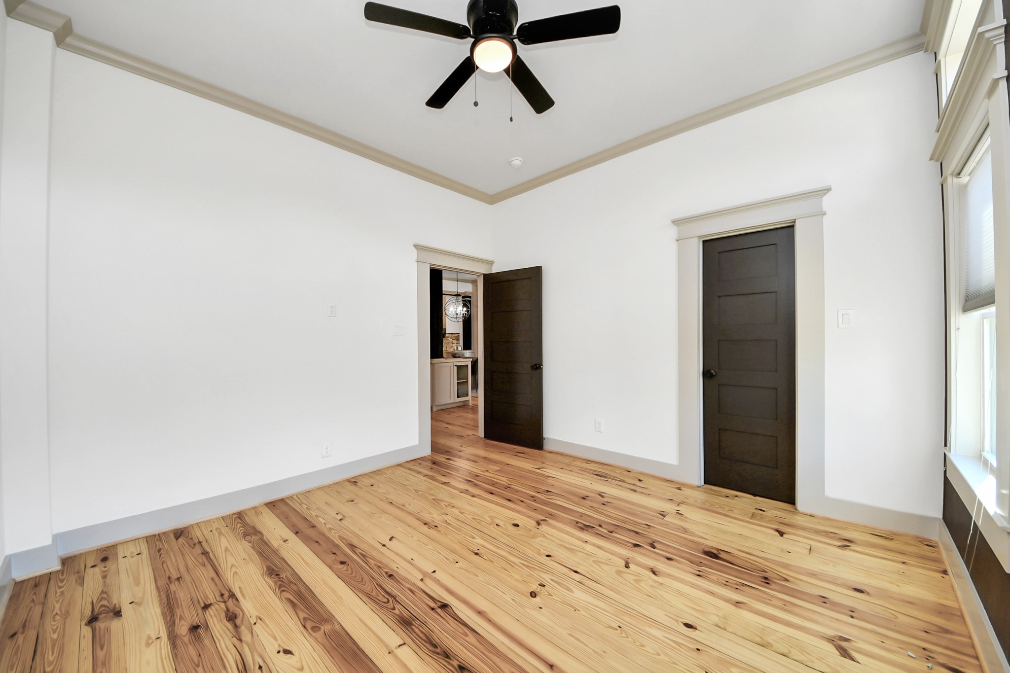 1202 Archer Street Houston, TX 77009 - Photo 29 of 46 This bright room is filled with natural light, highlighting the light wood flooring and a functional ceiling fan. Dark doors contrast elegantly with crisp white walls and trim, creating a modern, clean, and inviting atmosphere.