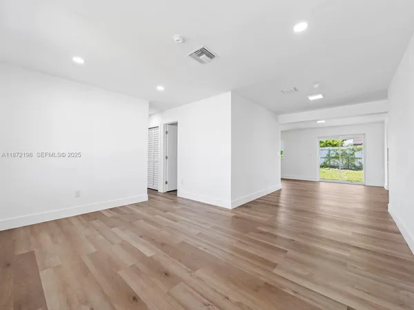 a view of an empty room with wooden floor and a window