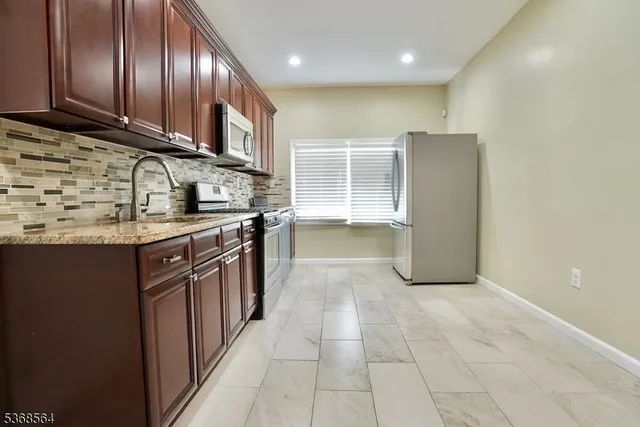 a kitchen with stainless steel appliances granite countertop a refrigerator a sink a stove top oven and wooden cabinets