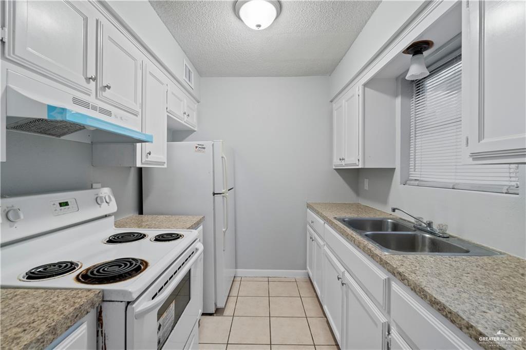 1701 West McIntyre Street, Unit 5 Edinburg, TX 78542 - Photo 8 of 15 Kitchen featuring white appliances, white cabinets, light tile patterned floors, a textured ceiling, and under cabinet range hood