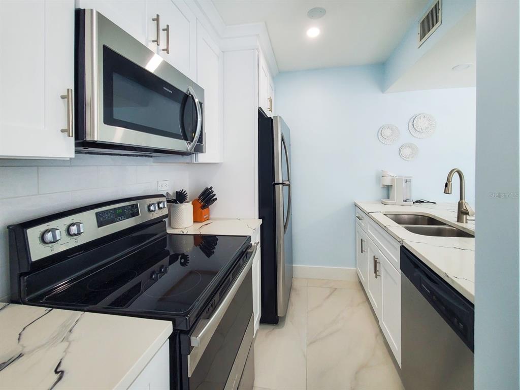 215 Medallion Boulevard, Unit G Madeira Beach, FL 33708 - Photo 7 of 29 a kitchen with stainless steel appliances a sink a stove and a microwave