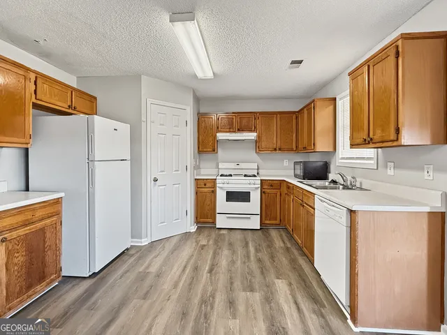 a kitchen with a refrigerator a stove top oven a sink dishwasher and wooden cabinets with wooden floor