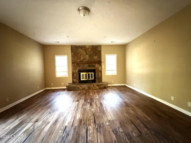 an empty room with wooden floor a fireplace and windows