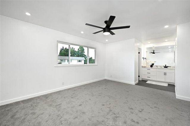 an empty room with a ceiling fan and kitchen view