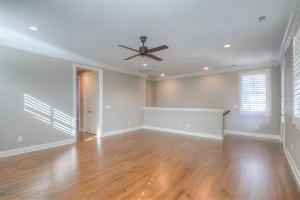 a view of an empty room with wooden floor and a ceiling fan