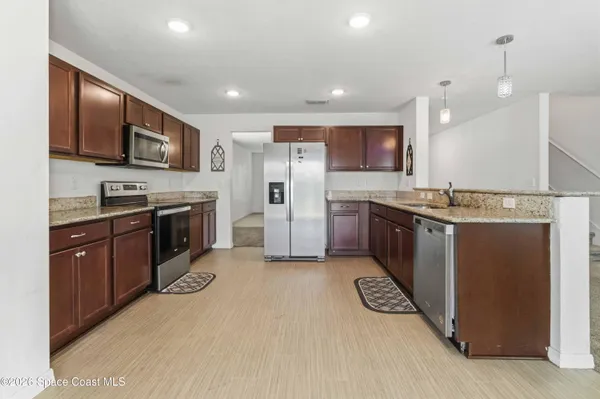 a kitchen with stainless steel appliances granite countertop a stove top oven a sink dishwasher a refrigerator and a microwave oven with large wooden cabinets