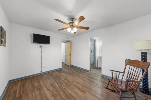 a view of an empty room with wooden floor and a ceiling fan