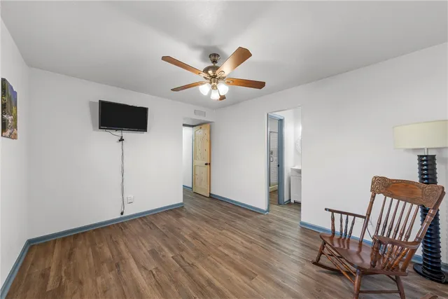 a view of an empty room with wooden floor and a ceiling fan