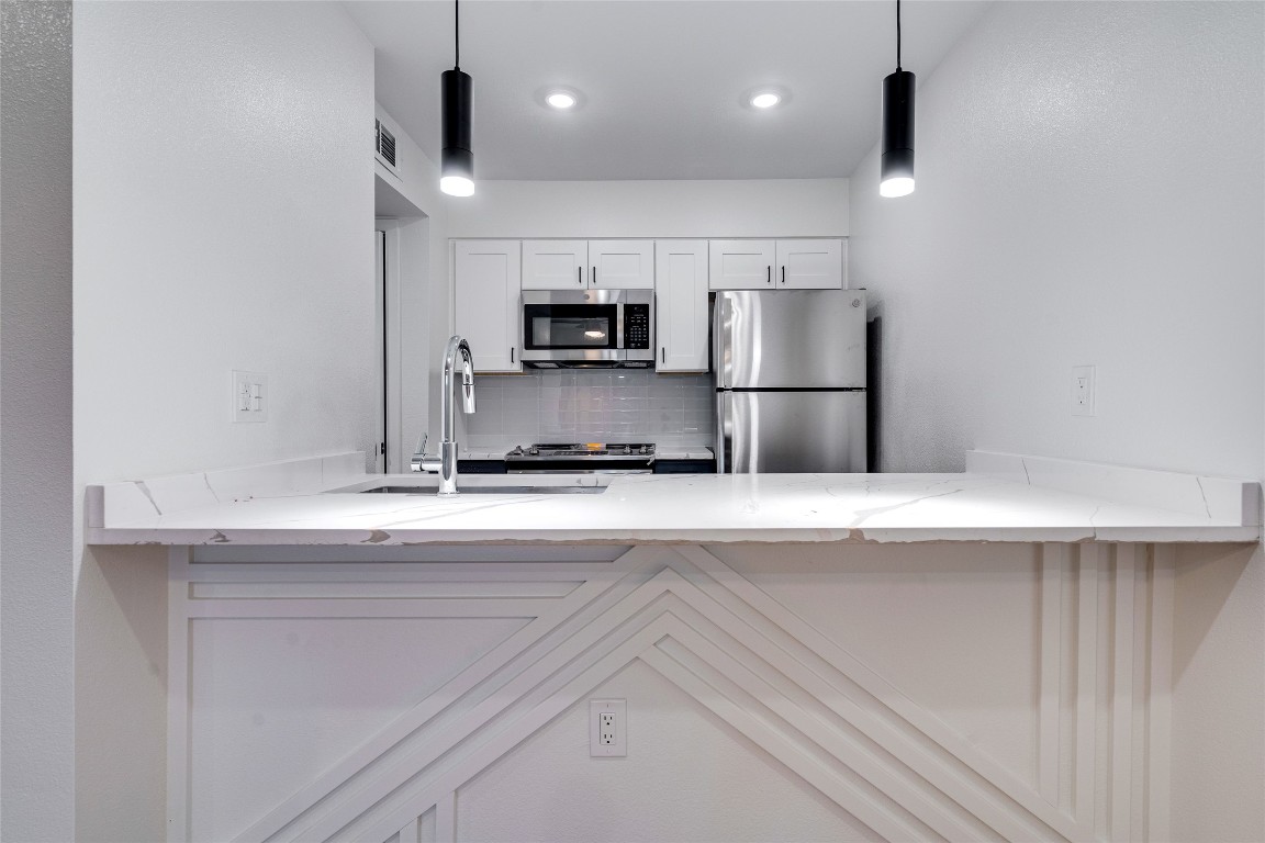 202 East 45th Street, Unit 202 Austin, TX 78751 - Photo 11 of 29 Kitchen with white cabinets, stainless steel appliances, hanging light fixtures, and light stone countertops