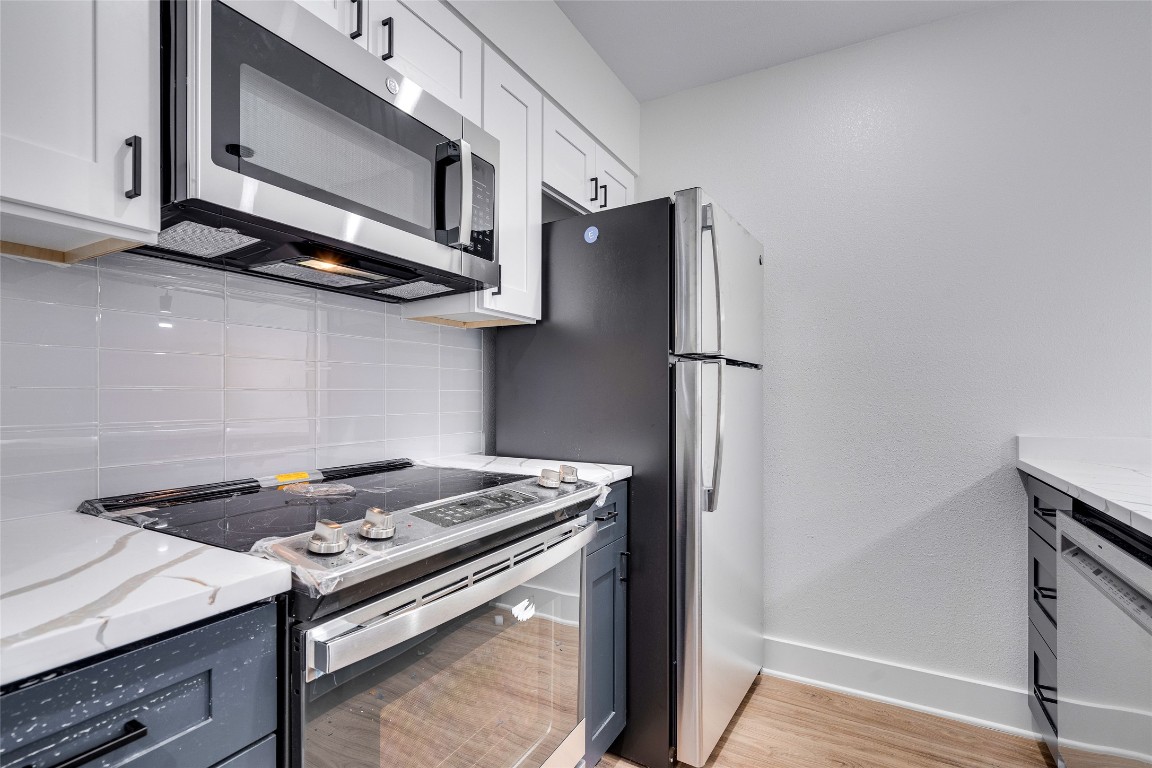 202 East 45th Street, Unit 202 Austin, TX 78751 - Photo 17 of 29 Kitchen featuring appliances with stainless steel finishes, decorative backsplash, light stone countertops, and white cabinetry