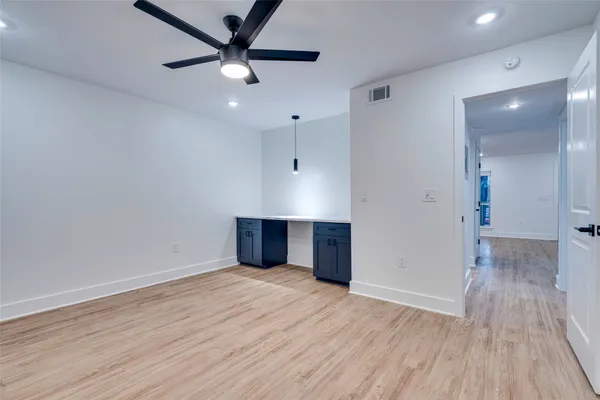 a view of an empty room with wooden floor and a ceiling fan