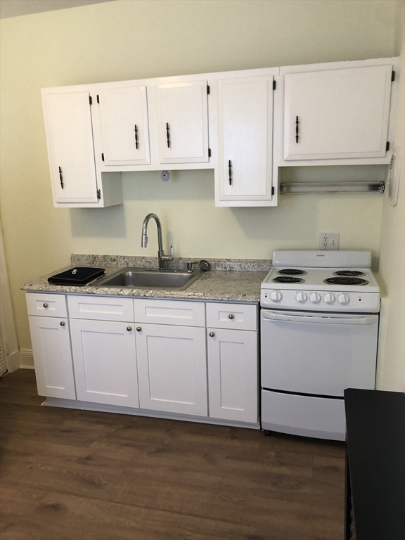 6 Rowley Street, Unit 1R Boston, MA 02122 - Photo 4 of 9 a kitchen with granite countertop white cabinets and white appliances
