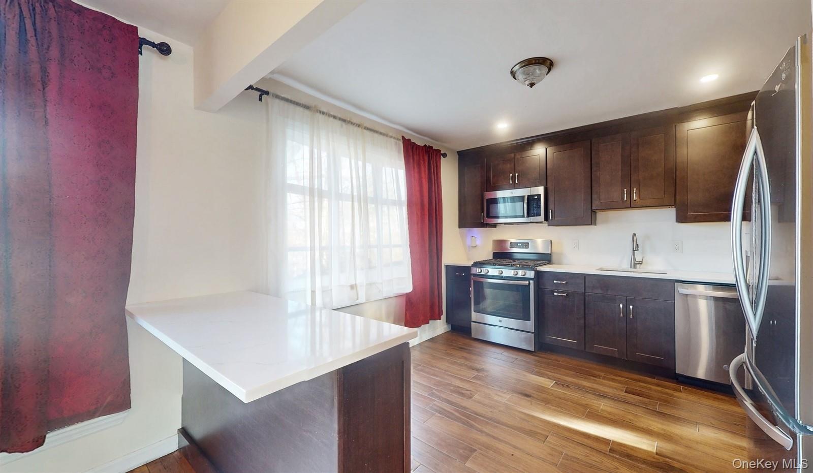 10 Rumbrook Road Elmsford, NY 10523 - Photo 7 of 25 Kitchen featuring kitchen peninsula, appliances with stainless steel finishes, a kitchen bar, sink, and light hardwood / wood-style floors