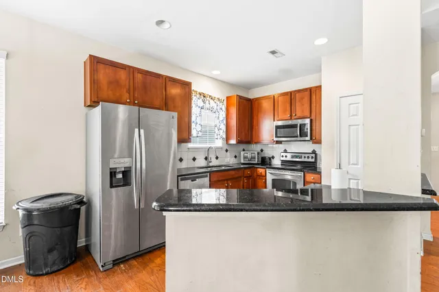 a kitchen with stainless steel appliances granite countertop a refrigerator a stove and a sink with wooden floor