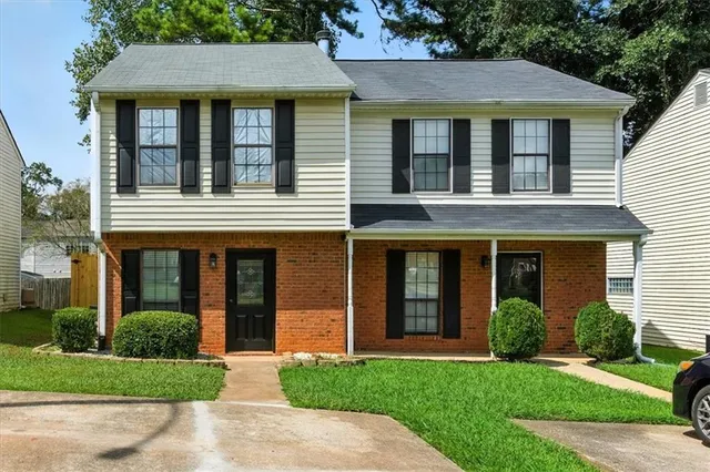 a view of a brick house with a yard plants and a large tree