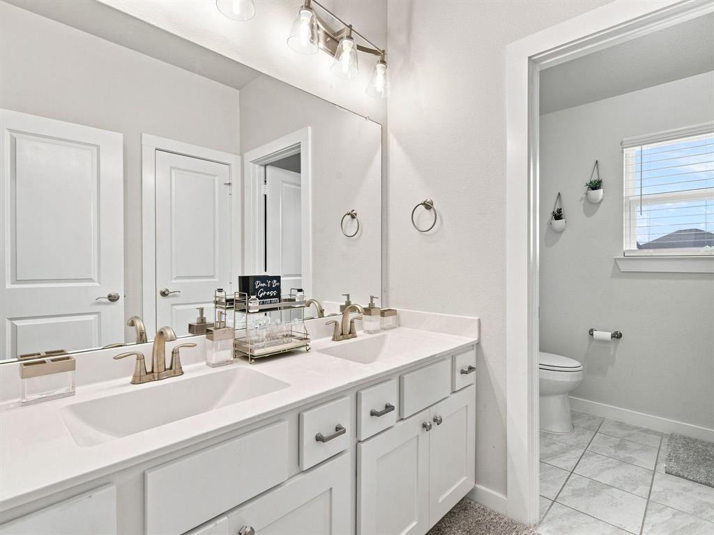 10216 Finch Road Sanger, TX 76266 - Photo 25 of 40 Dual basin vanity with brushed nickel fixtures and white cabinetry, complemented by a large wall-mounted mirror and overhead lighting