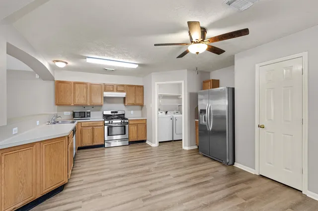 a kitchen with stainless steel appliances a refrigerator a sink dishwasher a stove and white cabinets with wooden floor