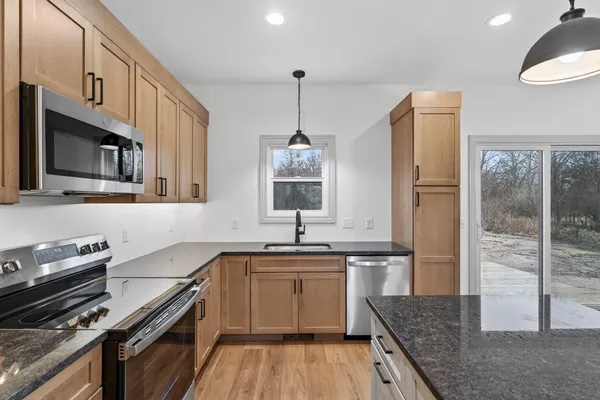 a kitchen with stainless steel appliances granite countertop a sink dishwasher a refrigerator and a fireplace with wooden floor