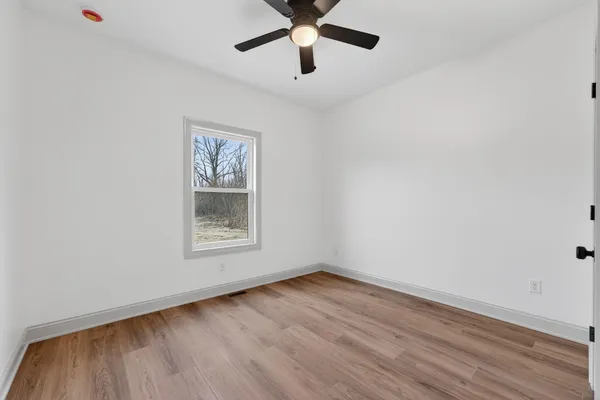 a view of empty room with wooden floor and fan