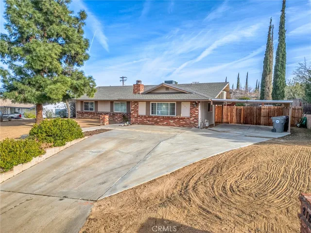 a view of a white house in front of a yard with plants and large tree