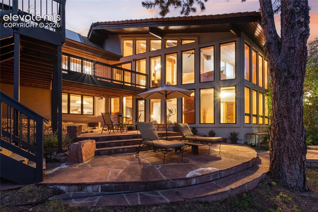Multi-level residence featuring extensive floor-to-ceiling windows, a spacious flagstone patio, and a second-story balcony with dark railings