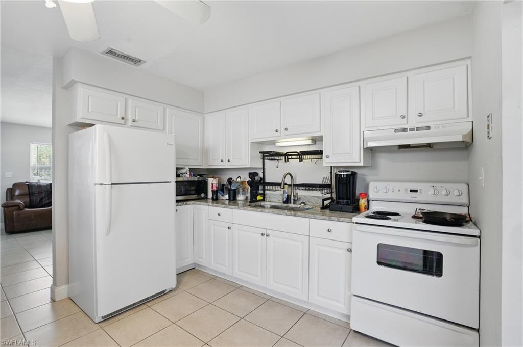 11580 Dean Street, Unit 582 Bonita Springs, FL 34135 - Photo 13 of 22 Kitchen with white appliances, under cabinet range hood, a sink, light tile patterned flooring, and white cabinetry