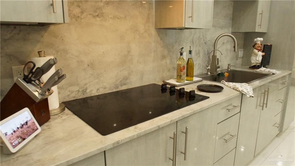 414 Ric Mar Street Edinburg, TX 78541 - Photo 19 of 36 Modern kitchen featuring a sleek black induction cooktop, light-toned cabinetry with brushed nickel hardware, a stainless steel undermount sink, and a high-arc faucet