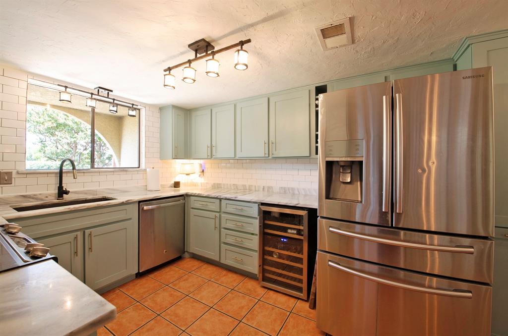 3915 Roma Court Rockwall, TX 75087 - Photo 11 of 40 Kitchen with appliances with stainless steel finishes, decorative backsplash, light tile patterned flooring, beverage cooler, and green cabinets