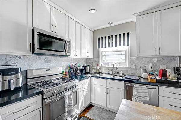 a kitchen with stainless steel appliances granite countertop white cabinets a sink dishwasher a stove and a microwave oven with cabinets