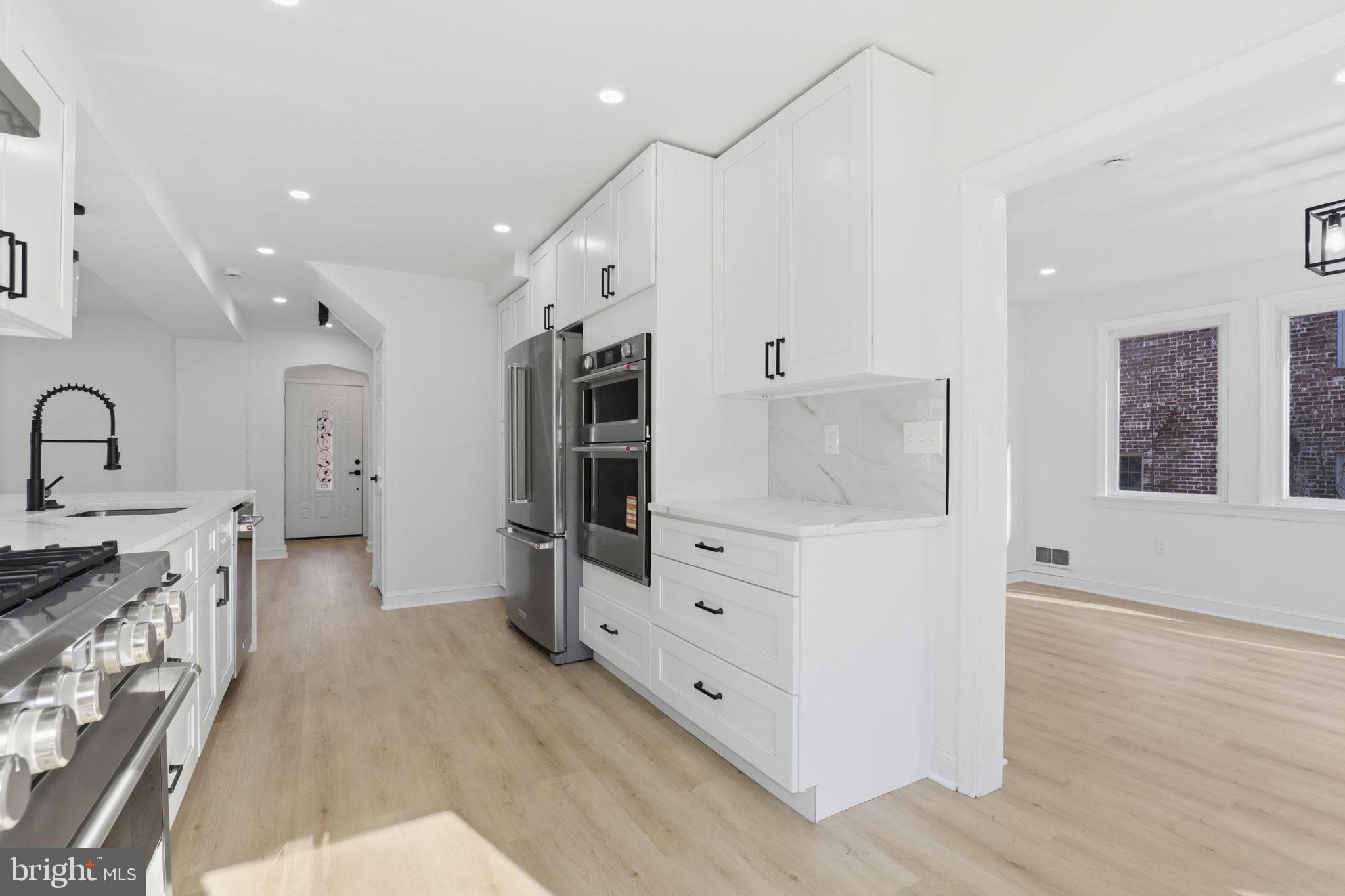 311 Ellsworth Drive Silver Spring, MD 20910 - Photo 17 of 65 a large white kitchen with stainless steel appliances a stove a sink dishwasher and a refrigerator with wooden floor