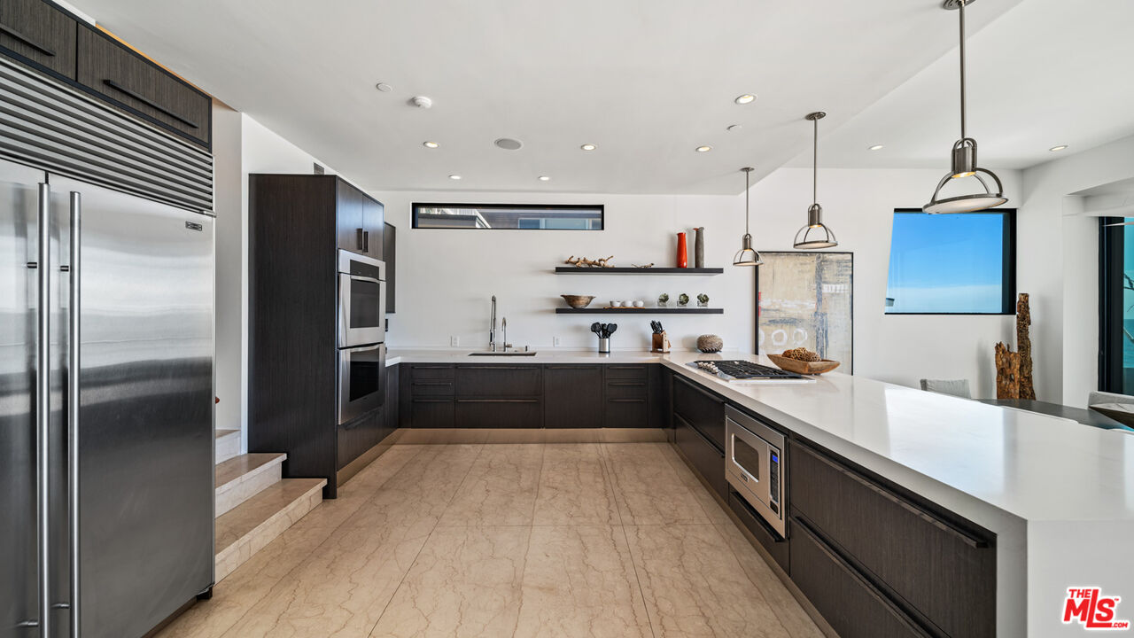 25250 Malibu Road Malibu, CA 90265 - Photo 24 of 66 a large kitchen with stainless steel appliances kitchen island granite countertop a refrigerator a sink dishwasher a stove and a dining table with wooden floor