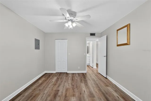 a view of an empty room with wooden floor and a fan