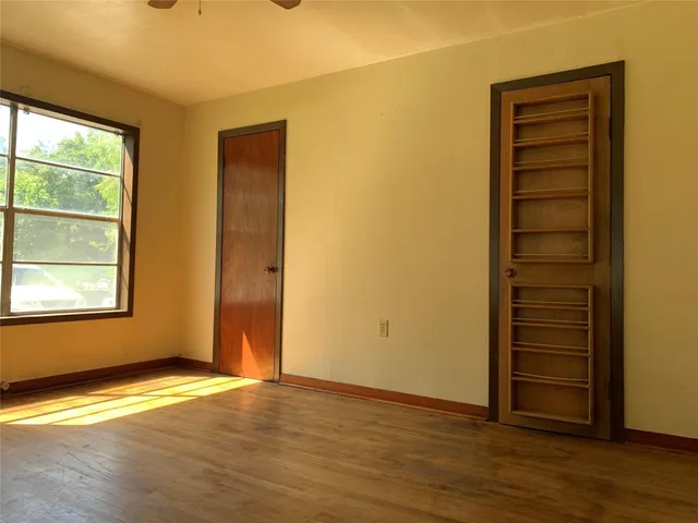 an empty room with wooden floor closet and windows