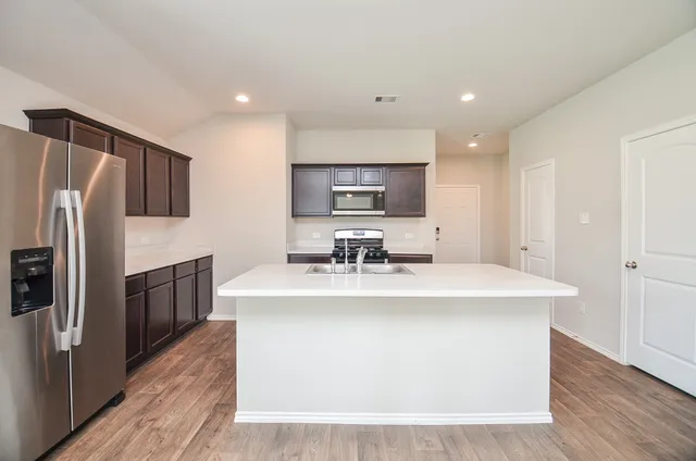 a view of kitchen with stainless steel appliances granite countertop a sink a stove a refrigerator and cabinets