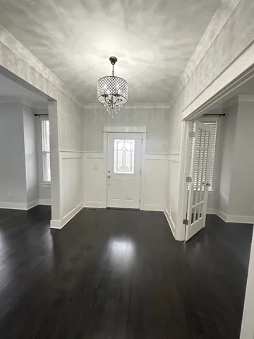 an empty room with wooden floor chandelier and windows