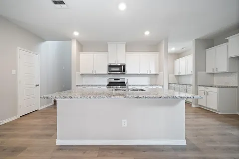 a kitchen with kitchen island granite countertop a stove top oven a sink and white cabinets