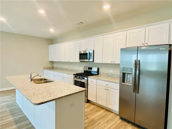 a kitchen with stainless steel appliances granite countertop a refrigerator a stove a sink a microwave and white cabinets
