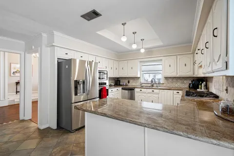 a kitchen with stainless steel appliances granite countertop a refrigerator a sink dishwasher a stove and white cabinets with wooden floor